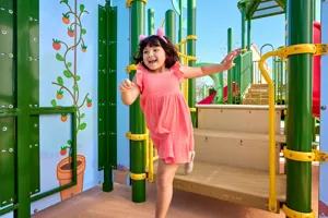 Una niña juega en la atracción de la Casa del Árbol de Peppa en Peppa Pig Theme Park en Dallas Fort Worth. Ella sube y explora la colorida y interactiva casa del árbol, sonriendo mientras disfruta del juego divertido e imaginativo en el animado entorno del parque.