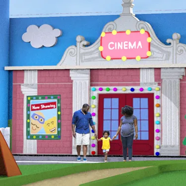 Una mamá y un papá se toman de la mano con su hijo frente al Cine en Peppa Pig Theme Park en Dallas Fort Worth. La familia sonríe mientras están juntos, disfrutando de la vibrante atmósfera del parque con el colorido cartel del cine al fondo.