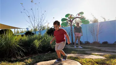 A mother and son play together at Madame Gazelle's Nature Trail attraction at Peppa Pig Theme Park in Dallas Fort Worth. They enjoy exploring the colorful and interactive nature trail, discovering fun features while surrounded by the vibrant, outdoor atmosphere of the park.
