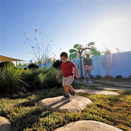 A mother and son play together at Madame Gazelle's Nature Trail attraction at Peppa Pig Theme Park in Dallas Fort Worth. They enjoy exploring the colorful and interactive nature trail, discovering fun features while surrounded by the vibrant, outdoor atmosphere of the park.