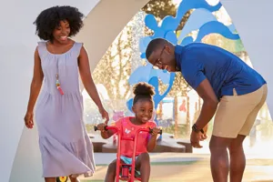 Una familia disfruta viendo a su hijo pedalear a través de Peppa’s Pedal Bike Tour y George’s Tricycle Trail en Peppa Pig Theme Park en Dallas Fort Worth. El niño pedalea felizmente a lo largo de los coloridos caminos, mientras los padres sonríen y animan, disfrutando de la divertida y pintoresca atmósfera del parque.