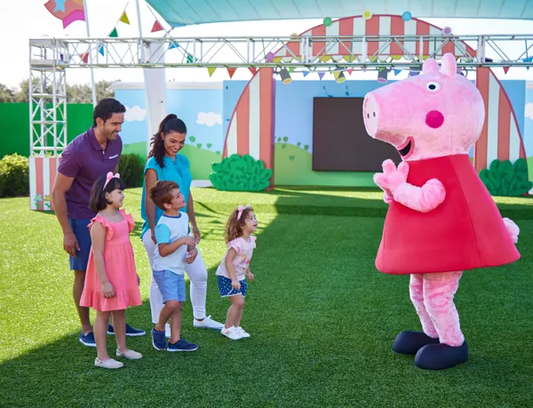 Una familia conoce a Peppa Pig en el Showtime Arena del Peppa Pig Theme Park, en Dallas Fort Worth. Los niños posan emocionados para una foto con sus personajes favoritos, creando momentos memorables en el ambiente lleno de diversión del parque.