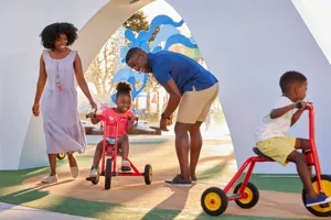 A family enjoys watching their children pedal through Peppa’s Pedal Bike Tour and George’s Tricycle Trail at Peppa Pig Theme Park in Dallas Fort Worth. The child rides happily along the colorful paths, while the parents smile and cheer, enjoying the fun and scenic atmosphere of the park.