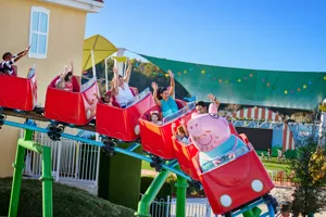 Visitors enjoy the thrill of Daddy Pig's Rollercoaster ride at Peppa Pig Theme Park in Dallas Fort Worth, smiling and laughing as they experience the exciting ride together.